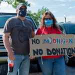 couple holds sign to save teh mohigan mascot